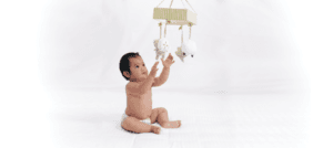 A baby sitting up and reaching for toys on a mobile to build fine motor skills.