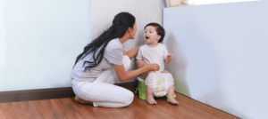 Mother guiding and encouraging a toddler on a small potty chair during basic potty training.