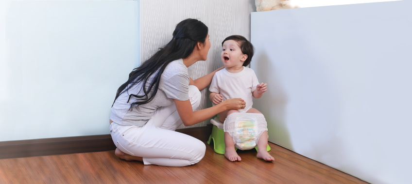 Mother guiding and encouraging a toddler on a small potty chair during basic potty training.