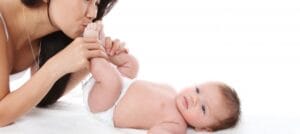 A mother holding and kissing her baby's feet while checking baby developmental milestones.