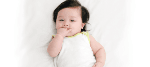 A teething baby lying in bed and chewing on fingers to soothe bedtime discomfort.